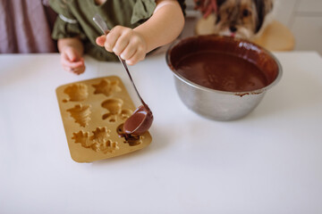 Little girl pours chocolate dough into Christmas silicone molds on the table
