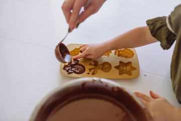 Little girl and mom pour chocolate dough into Christmas silicone molds on the table.