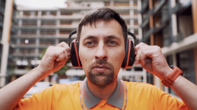 Man wearing safety equipment hearing protection. Worker wearing noise cancelling ear defenders or ear muffs. Construction builder puts on protect ears with headphones. Taking care safety during work