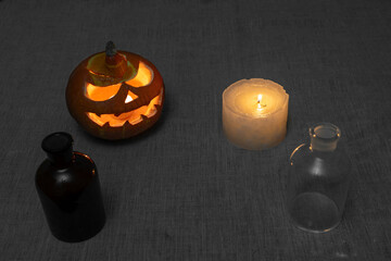 Carved pumpkin lantern with candle and chemical bottles on gray linen cloth