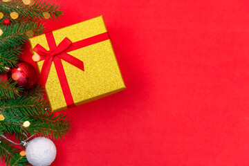 Gift box with a red bow, spruce branch and Christmas balls with snow and lights on a red background close up with copy space, top view. Christmas or New Year background.