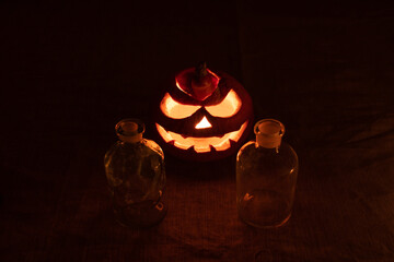 Carved pumpkin lantern with candle and chemical bottles on gray linen cloth