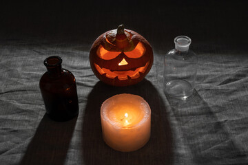 Carved pumpkin lantern with candle and chemical bottles on gray linen cloth