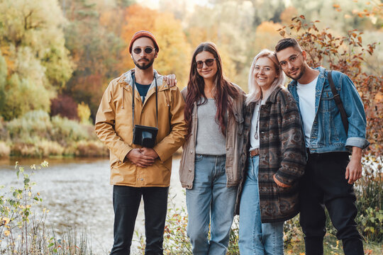 Joyful group of best friends posing in background of autumn forest and lake in lovely nature landscape in daytime.