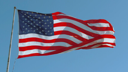 American USA flag on a flagpole waving in the wind against a clear blue sky on a sunny day.