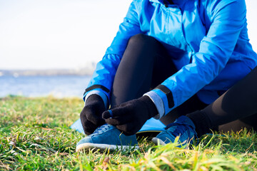 Woman tightening laces on sneakers, no face, preparing for outdoor workout in autumn in warm clothes
