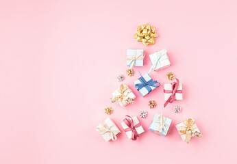 Christmas ornamets and gift boxes laid out in shape of Christmas tree on pink background
