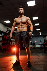 Fototapeta na wymiar Handsome man with big muscles, posing at the camera in the gym. View from below. Dark light background.