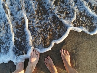 Ein Paar lässt seine Füße von einer schaumigen Welle bedecken - Fernweh - Urlaubsreif - Meer - Sand - Wellen