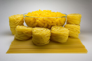 Fusilli in a deep glass plate and fettuccine on a white background.