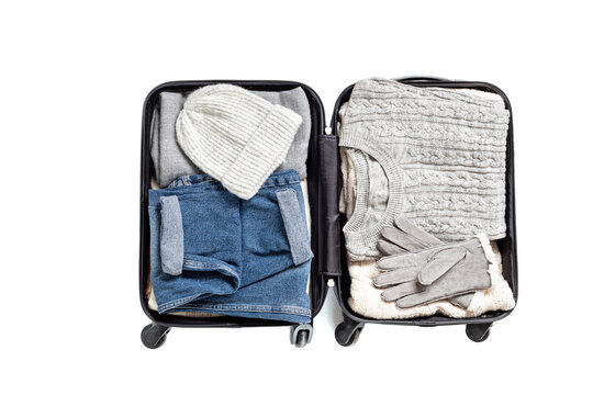 Flat lay with open suitcase with casual clothes for autumn, winter vacations over white background