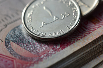 Extreme close up of one Dirham coin placed over hundred dirham note. Currency and coins of United...