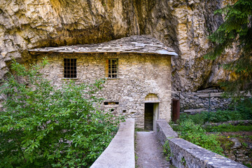 The old stone bridge on the Dora of Verney stream with an abandoned building built in the rock of the mountain in summer, Pr&eacute;-Saint-Didier, Aosta, Italy