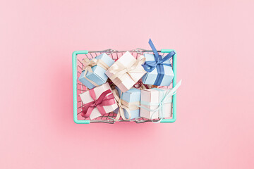 Christmas gift boxes in shopping basket on pink background. Winter holidays gifts shopping