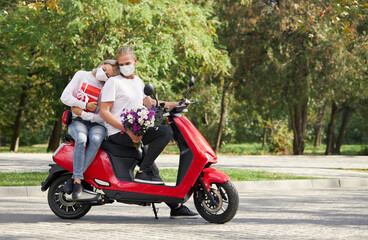 Fototapeta na wymiar Young couple in protective masks on a red retro scooter on a romantic date during the coronavirus pandemic