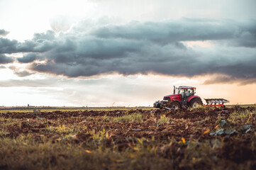 Tractor plowing the fields in the countryside by sunset. Agricultural tractor plowing the field. Red Tractor with plow. Sunset over the autumn field. © Peter