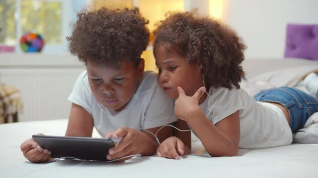 Portrait of adorable african boy and girl kids watching cartoon in earphones on digital tablet
