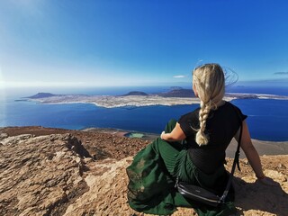 Young blond woman with green skirt is sitting on a stone and watching the sea horizont - holiday relax, Frau in grünem Kleid genießt wundervollen Ausblick auf den Horizont, Insel, Meer