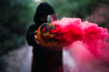 Chico joven con mascarilla por covid 19 con calabaza de halloween con humo de color