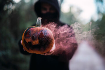 Obraz premium Chico joven con mascarilla por covid 19 con calabaza de halloween con humo de color