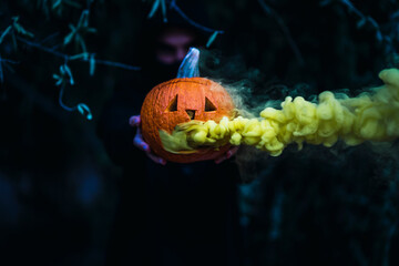 Chico joven con mascarilla por covid 19 con calabaza de halloween con humo amarillo