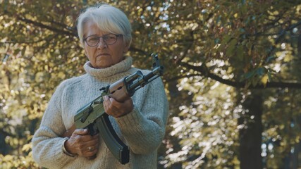Elderly gray haired woman holding a gun in her hands. War or revolution concept. High quality photo