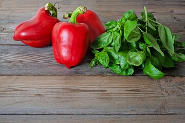Ripe red bell pepper (paprika) with fresh green basil on wooden background, healthy food concept, vegan food.
