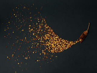 Pile crushed red cayenne pepper, dried chili flakes and seeds on a black background. Homemade...