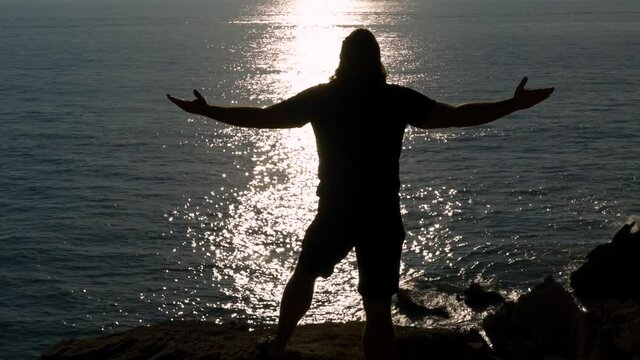 Silueta de hombre en un acantilado frente al reflejo del sol en el mar lavantando los brazos un d&iacute;a sensacional. Desde Conil, C&aacute;diz, Andaluc&iacute;a, Espa&ntilde;a, Europa.