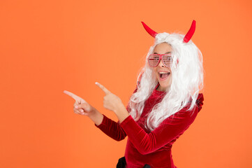 Fototapeta na wymiar happy halloween. smiling child in devil horns and party glasses. kid has long white hair wig. childhood happiness. teen girl ready to celebrate party. funny red imp horns. pointing finger