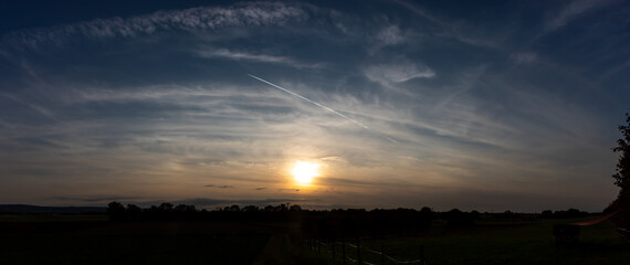 panorama view over farmland at sunset, field with fence in the foreground, dirt road between the...