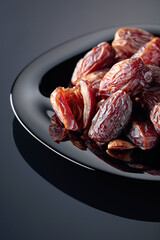 Dried sweet dates on a black plate.