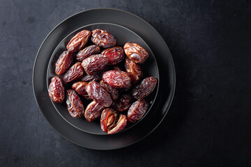 Dried sweet dates on a black plate.