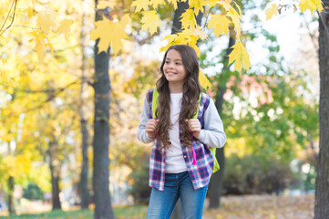 perfect autumn day of cheerful kid with school bag walking in fall season park in good weather, happy childhood