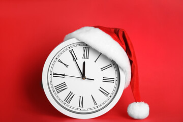 Clock with Santa hat showing five minutes until midnight on red background. New Year countdown