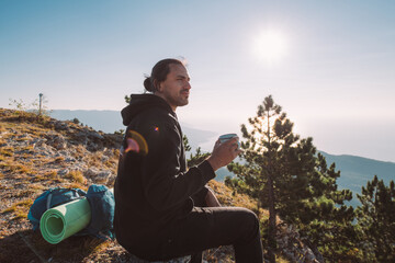 Male tourist drinks tea on the top of the mountain at sunrise