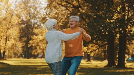Happy old couple dancing in park. Senior man flirting with elderly woman. Romance at old age autumn day. High quality photo