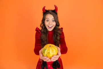 surprised child in devil horns. kid hold pumpkin vegetable. traditional holiday food and autumn...