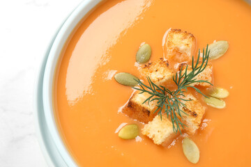 Tasty creamy pumpkin soup with croutons, seeds and dill in bowl on white background, closeup