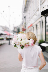 A bouquet of peonies in the hand of a girl. Happy girl with a bouquet of peonies walking through a deserted city in the early morning