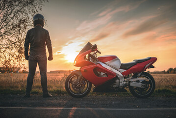 Motorbiker is standing on the countryside road and is looking on the sunset.
