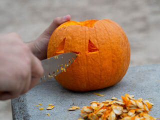 Hombre joven con tatuajes diseñando una calabaza de halloween con un cuchillo