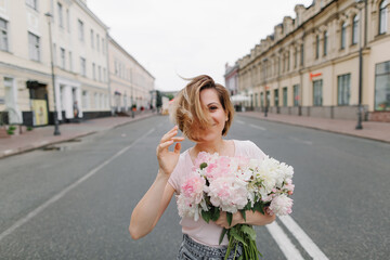Fototapeta premium Happy girl with a bouquet of peonies walking through a deserted city in the early morning