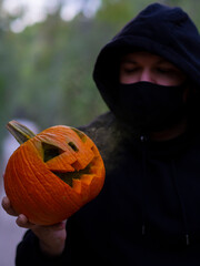 Hombre encapuchado con mascarilla sujetando una calabaza con humo de colores 