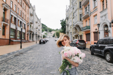 Happy girl with a bouquet of peonies walking through a deserted city in the early morning