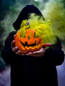 Hombre encapuchado con mascarilla sujetando una calabaza con humo de colores 