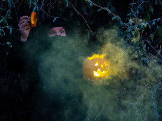 Hombre encapuchado con mascarilla sujetando una calabaza con humo de colores 