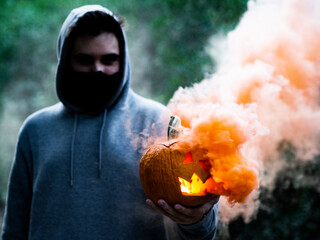 Hombre joven con mascarilla sujetando una calabaza con humo de colores