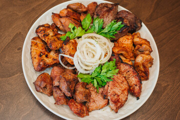 Fried meat on a white plate with onions and herbs. Appetizing barbecue. Chunks of beef on a platter. On a dark wooden background