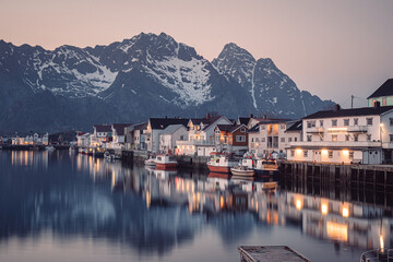 Naklejka premium charming view of small village at night after sunset in Lofoten. Water surface of harbor was quiet and peaceful, so the reflection of mountains and houses was clear and amazing